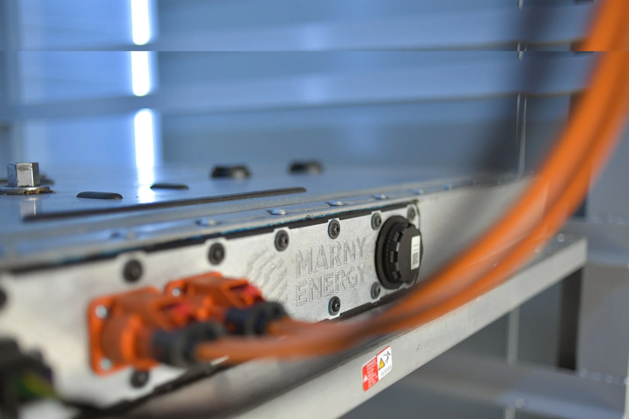Close-up of a second-life EV battery module with the MARNY ENERGY logo embossed in metal and orange high-voltage cabling